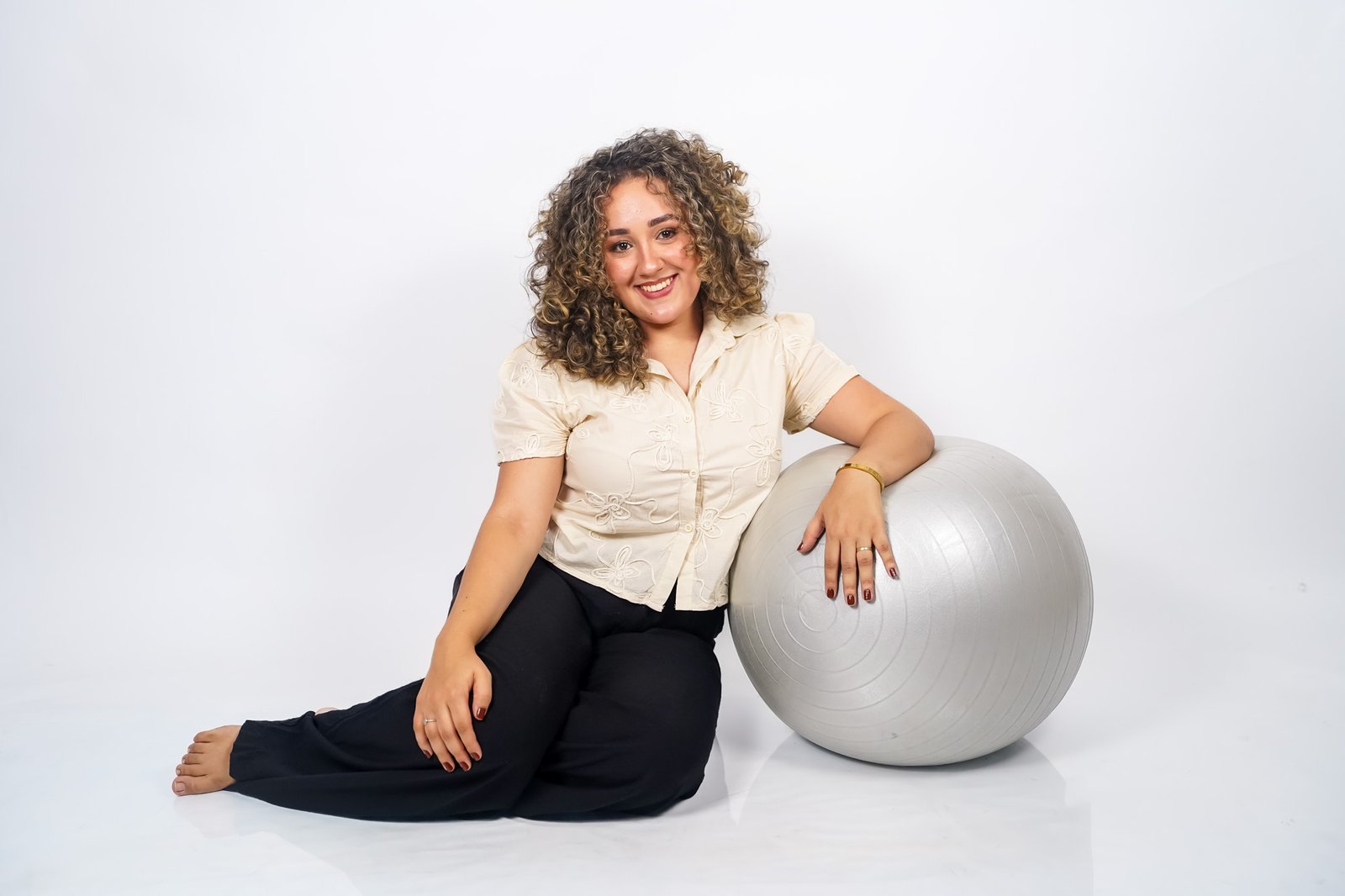 Mulher Fisioterapeuta sentada no chão apoiada sobre uma bola de exercícios